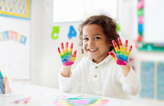 A child with rainbow coloured paint on their hands.