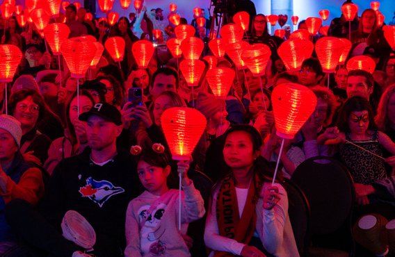 A crowd of people sitting and holding up red lanterns at a Light The Night event.